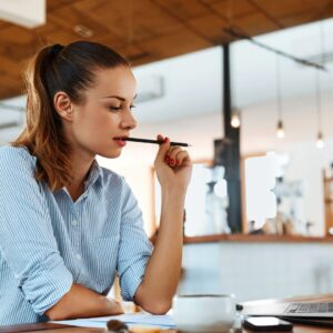 woman chews on pencil while looking at laptop on desk 