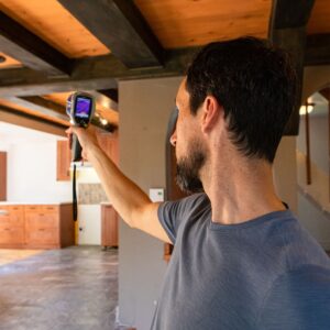 man holds up a moisture detection device inside a vacant house