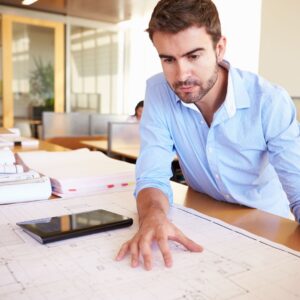 man in collared shirt looks over house plans on table